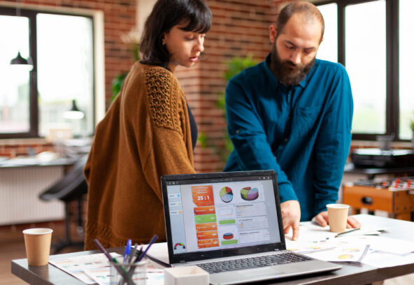 Businesspeople analyzing management documents discussing company strategy Businesspeople analyzing management documents discussing company strategy while brainstorming ideas for business project in startup office. Laptop computer with marketing data chart on screen