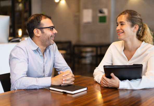 Happy mid adult manager talking to young female client Happy mid adult manager talking to young female client. Caucasian executive wearing glasses sitting at table and talking to female colleague. Job interview or meeting with client concept