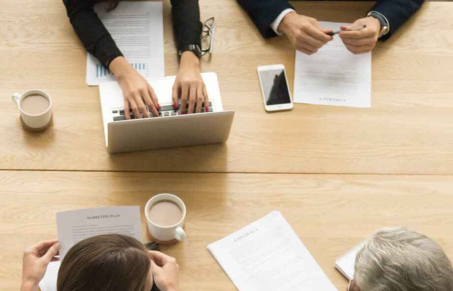 Diverse business colleagues working together talking planning at meeting table, multiracial young and senior people preparing for contract negotiations talking during teamwork, vertical top view