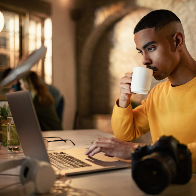Young black businessman drinking coffee while working late on a computer in the office.
