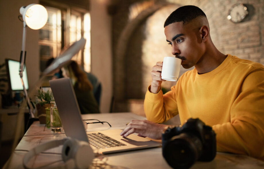 Young black businessman drinking coffee while working late on a computer in the office.